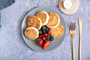 Fried cheesecakes on a plate with sour cream, berries and powdered sugar top view