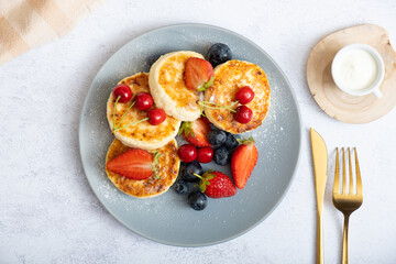Fried cheesecakes on a plate with sour cream, berries and powdered sugar top view