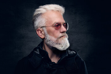 Studio shot of handsome elderly man with modern hairstyle dressed in black attire with sunglasses.