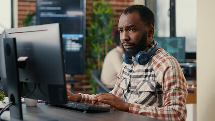Portrait of focused african american programer wearing wireless headphones working looking at...