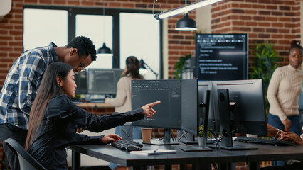 Mixed team of software developers analyzing source code pointing at screens comparing algorithm...