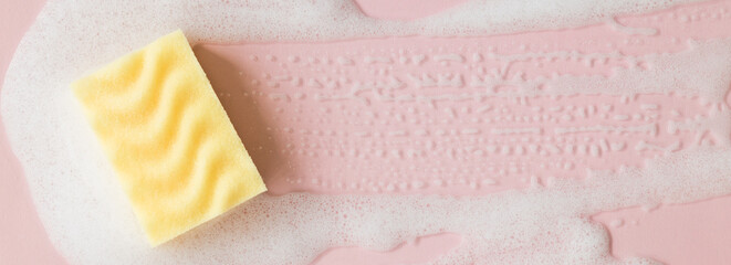 Yellow sponge with detergent foam on pink background, close up. Cleaning concept