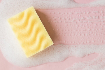 Yellow sponge with detergent foam on pink background, close up. Cleaning concept - obrazy, fototapety, plakaty