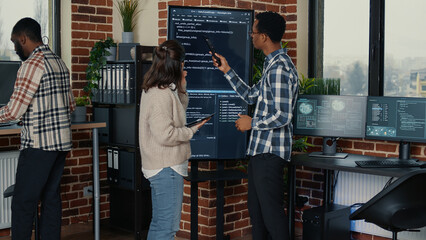 Team of database admins analyzing source code on wall screen tv comparing errors using digital...