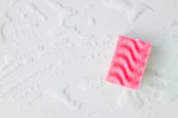 Pink sponge with detergent foam on white background, close up. Cleaning concept