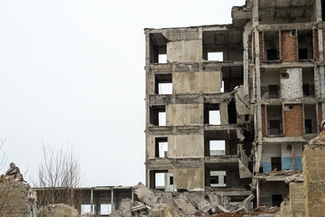 A ruined building against a gray sky with piles of concrete rubble and protruding piles in the...
