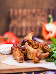Spicy Homemade Buffalo wings with sauce, beer, tomatoes and herbs on a wooden board. Restaurant serving.