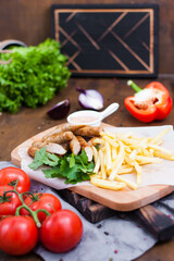 Fried sausages served on a board with French fries, sauce and herbs