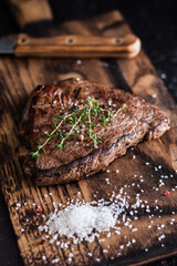 Beef tenderloin steak with salt and herbs on a wooden board on a dark background