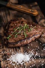 Beef tenderloin steak with salt and herbs on a wooden board on a dark background