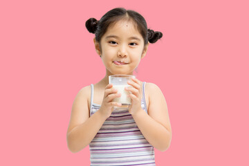 Smiling little Asian girl drinking milk isolated on pink background.