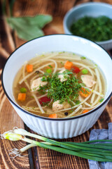 Chicken soup with noodles and vegetables in a white bowl on a rustic wooden background