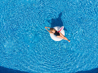 woman relaxing in pool float unicorn inflatable ring floating on turquoise pool water. Aerial top view from drone