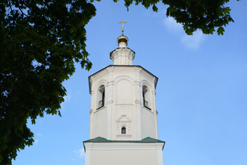 Close-up of white church with cross against blue sky, an old monastery in frame of trees outdoors