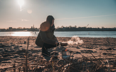 Young asian woman with warm clothes on is cooking with outdoor cooker on Harriersand beach at a...