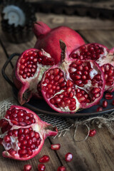 beautiful pomegranate fruits with pits on a metal plate on a wooden table in a dark key in rustic style