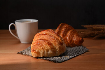 Delicious, fresh croissants and coffee cup on wooden table for homemade breakfast