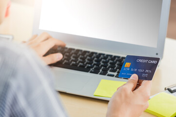 Asian business man hand holding credit card and typing entering security code on a laptop computer for process payment online shopping on the internet at the home office