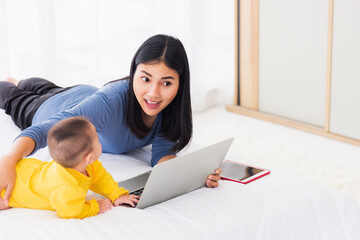 Fototapeta premium Asian new young beautiful mother finding and reads information on a laptop for milk mixing on a bottle in the bedroom at home