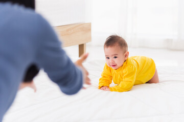 Asian happy young mother have fun learn walking crawling his daughter baby indoors bedroom at home. The mom playing with her little baby to crawl, two family