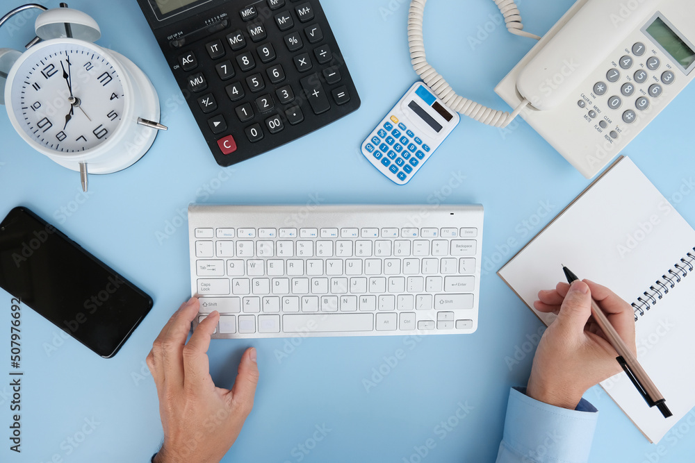 Poster hand typing on keyboard, flat lay, top view with copy space. a bank notepad and a pen are on top of 