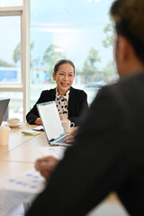 Positive Asian aged female boss or executive manager talking with male financial analysts