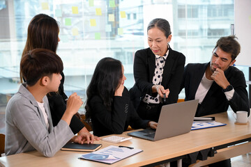 A group of Asian businesspeople listens intently to her professional aged female boss
