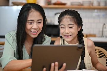 Happy asian mom and young daughter enjoy watching kids show together via tablet