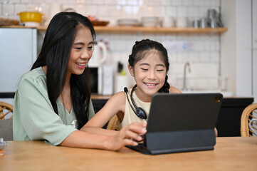 Beautiful asian mom and lovely daughter looking at tablet screen together