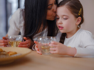 Family drinking tea with cookies on kitchen at home. Mother and daughter having fun, happy moment together at home.
