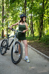 Fototapeta premium Young sexy woman wear green short dress rides a bicycle in the forest, spend time on summer day