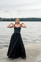 Fototapeta na wymiar Beautiful young lady in a long dark dress on background of sky and water