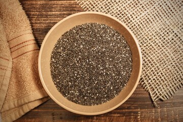 A cup full of chia seeds. chia seeds in a bowl with table cloths aside on wooden table.