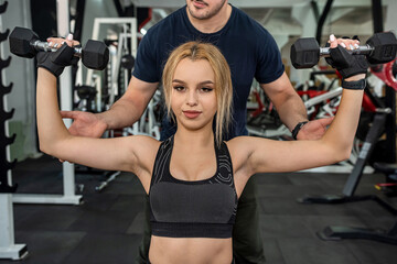 Fototapeta premium young trainer with inflated biceps trains a young cute brunette client for body health.