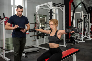 Fototapeta na wymiar male trainer help her woman client working with dumbbell weights at gym