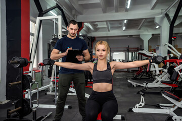 Fototapeta na wymiar Personal male instructor helping woman doing exercise with heavy dumbbells