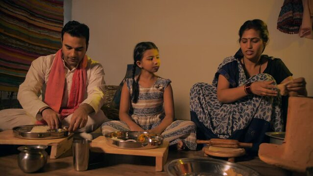 Indian village housewife happily serving chapatis to her husband and daughter. Medium shot of a middle-aged woman serving chapatis to her family during lunch/dinner time - lifestyle concept