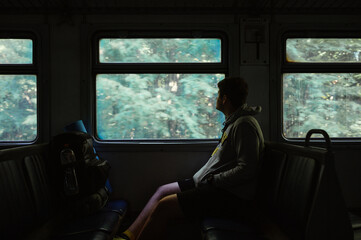 A male tourist rides in a dark train through the woods and looks out the window