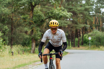 Obraz premium Male professional cyclist in sportswear rides out of town on an asphalt road with a serious face.