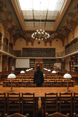 A woman's back stands in an empty public atmospheric library.