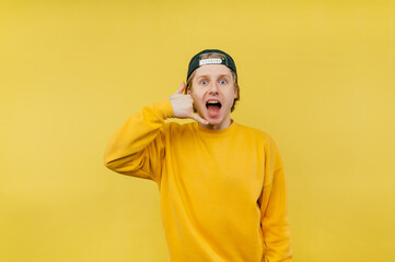 Joyful guy in a cap and casual clothes shows a ring gesture with his fingers and looks at the camera with an emotional face.