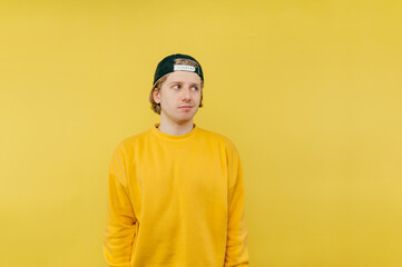 Handsome young man in a cap and yellow sweatshirt stands on a colored background and looks away.