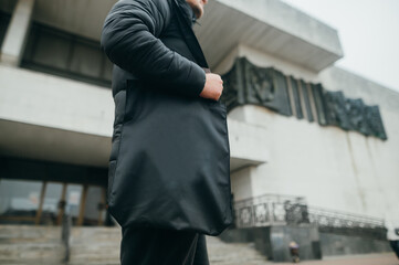 A man with a black eco bag in his hands walks around the city in cool weather.