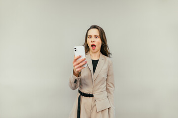 Shocked business woman looking at smartphone screen with surprised face on beige background. Isolated