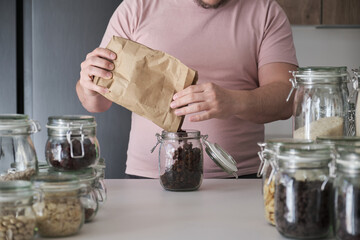 Unrecognizable latin man filling up a jar with raisins from a paper bag. Food in bulk delivery.
