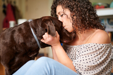 tender close-up portrait of a young woman holding her dog by the head and giving it a big kiss on the forehead.