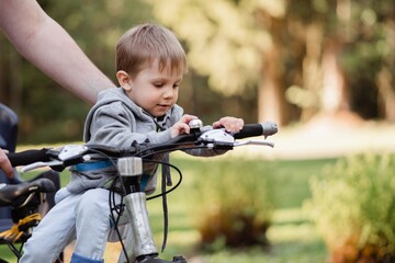 Cute little caucasian boy sitting on beach by father bicycle. Family weekend in countryside