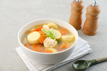 Clear soup with egg tofu, carrot and shrimp meatballs. Served in white bowl on grey background.
