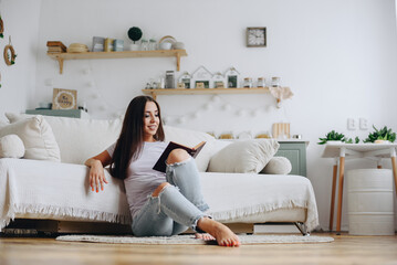 smiling girl reading book on sofa at home. girl sits on floor with book in her hands.