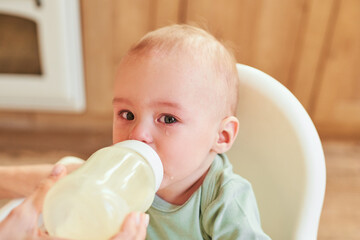 Portrait of a crying baby drinking milk from a baby bottle.